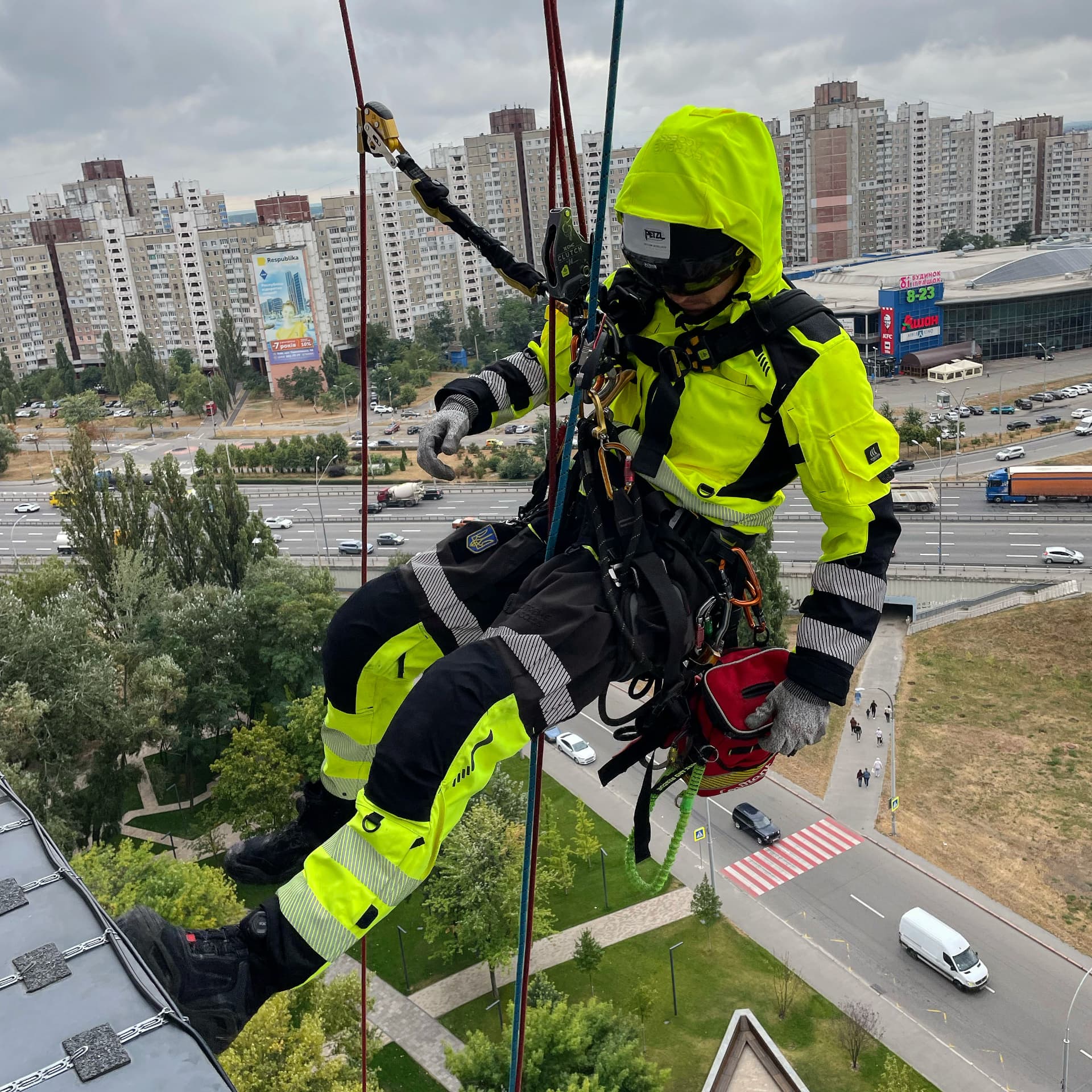 Technician in hi-vis Extreme Access workwear suspended on ropes above city streets