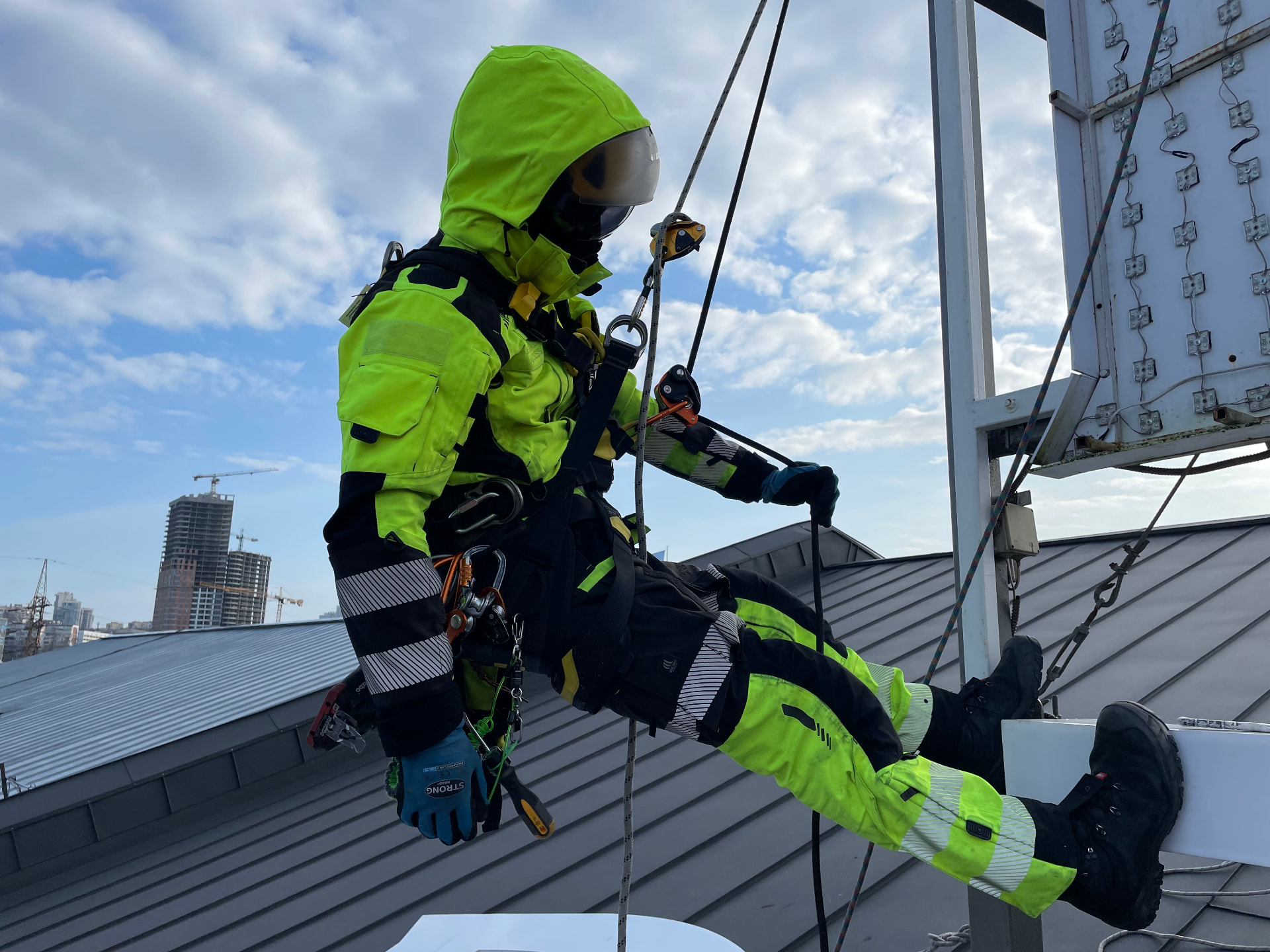 Working rope access technician in ULTIMATE hi-vis gear suspended beside a city building